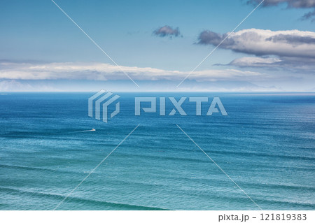 Aerial, landscape, and copyspace view of the ocean and beach waves against a cloudy climate and blue sky in summer. Beautiful, scenic, and top view of the calm and relaxing sea on the coast in nature 121819383