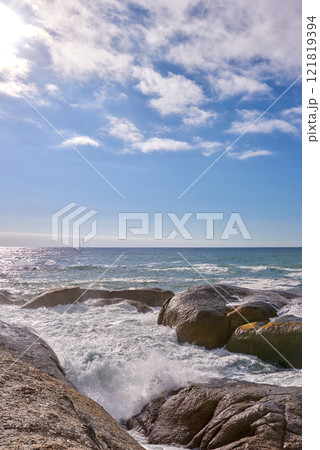 Waves crashing against rocks in the ocean under a blue cloudy sky with copy space. Scenic landscape of boulders or big stones in the sea at a popular summer location in Cape Town, South Africa 121819394