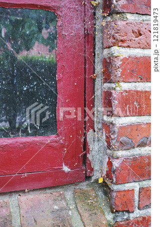 Closeup of abandoned red window covered in spiderwebs from neglect, poverty and economic crisis. Empty, old and dirty residential brick building or home in village with broken frame on the windowsill 121819473