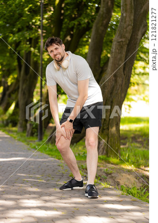 Young runner man athlete with muscle pain massaging stretching, trauma injury while jogging in park 121821277