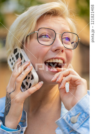 Happy young Caucasian blonde woman with short hair talking gossip on smartphone on city street 121821408