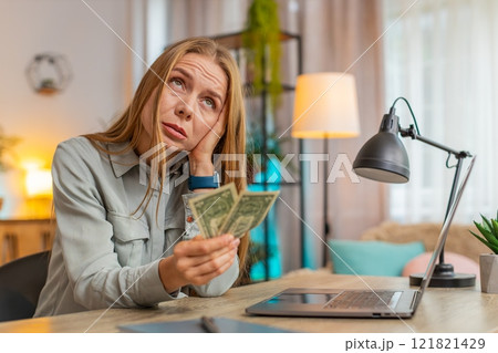 Upset Caucasian woman freelancer counting dollar cash insufficient amount of money sitting at table Upset Caucasian woman freelancer counting dollar cash insufficient amount of money sitting at table 121821429