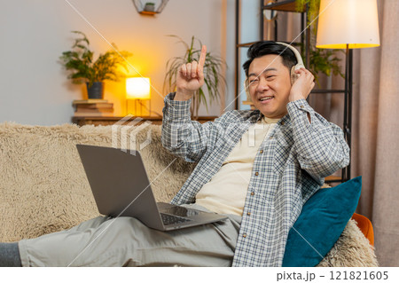 Happy relaxed overjoyed Chinese middle-aged man in wireless headphones listening to music on sofa 121821605
