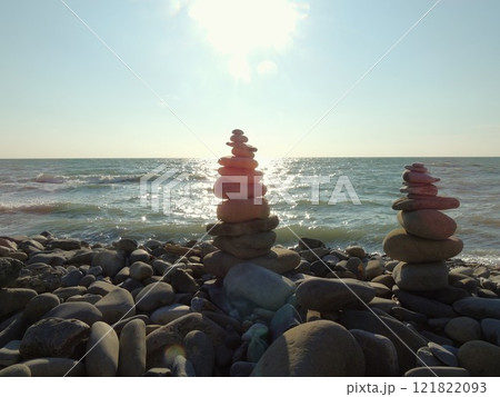 two pyramids of rounded stones on a sunny rocky coast of the sea or ocean, as a symbol of balance, tranquility and harmony, a stone tower of cobblestones on the seashore on a sunny day 121822093