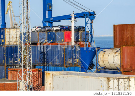 Cargo and tank containers stacked with cars on top on bulk carrier in sea port on sunny day. Maritime logistics, transportation, commercial seaport, shipping containers in various colors, cargo 121822150