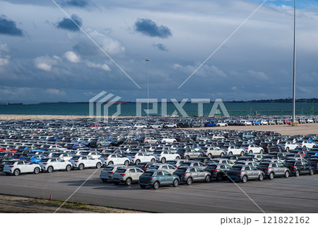 Aerial view of a vast parking lot at seaport cargo terminal. Rows of new vehicles fill the space, creating a colorful mosaic. Cars await shipment to global destinations via nearby Ro-Ro vessels. Scale 121822162
