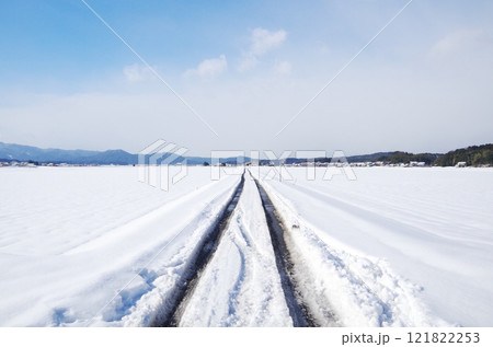 農道に積もった雪が晴天の気温上昇で少しずつ融けて自動車のタイヤ跡でアスファルト路面が露出している状態 121822253