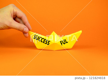 Successful symbol. Concept word Successful on beautiful yellow paper boat. Beautiful orange background. Businessman hand. Business successful concept. Copy space. Successful symbol. Concept word Successful on beautiful yellow paper boat. Beautiful orange background. Businessman hand. Business successful concept. Copy space. 121824818