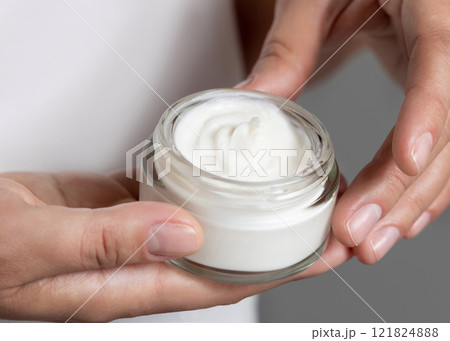 Female hand holding opened face cream jar against white t-shirt close up. Beauty concept Female hand holding opened face cream jar against white t-shirt close up. Beauty concept 121824888