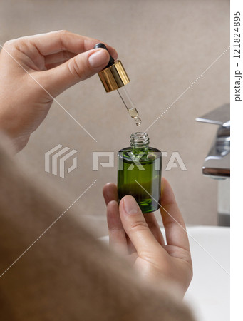 Closeup of woman in brown bathrobe opening green dropper bottle, cosmetic mockup Closeup of woman in brown bathrobe opening green dropper bottle, cosmetic mockup 121824895
