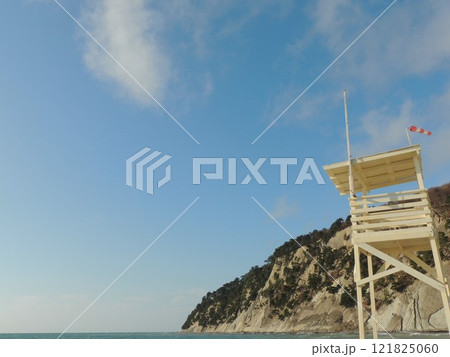 observation tower on empty beach made of light wood with red and white flag showing strong wind against background of cliff on seashore on sunny day observation tower on empty beach made of light wood with red and white flag showing strong wind against background of cliff on seashore on sunny day 121825060