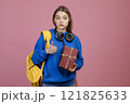 Front view of young pretty student standing, holding present. Beautiful schoolgirl wearing casual clothes, looking at camera, showing super. Isolated on pink studio background. 121825633