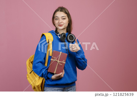 Front view of teenage girl standing, holding present, gift box. Beautiful schoolgirl looking at camera, smiling, showing super. Concept of school, college, university and youth. Front view of teenage girl standing, holding present, gift box. Beautiful schoolgirl looking at camera, smiling, showing super. Concept of school, college, university and youth. 121825639