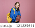 Front view of angry schoolgirl standing, holding bunch of old books. Pretty young student wearing stylish cothes, looking at camera. Concept of education, studying and youth. 121825641