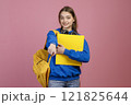Front view of brunette female brunette standing, holding yellow backpack and rucksack. Pretty schoolgirl wearing blue khudi and jeans, pointing by finger. Concept of youth life. 121825644