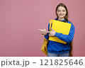 Front view of pretty schoolgirl standing with folder, looking at camera. Beautiful young female smiling, happy, glad, pointing by fingers. Isolated on pink studio background. 121825646