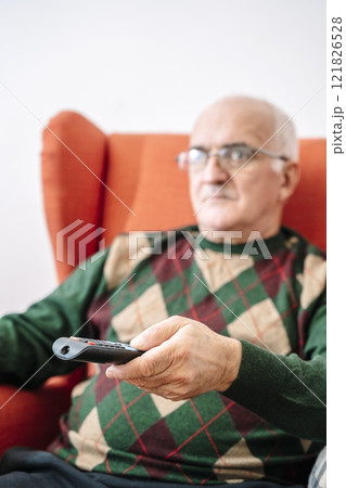 Elderly man holding TV remote control at home. Grandfather watching TV in living room 121826528