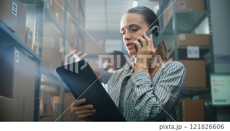 Female Manager Talks with Client on Phone, Uses Tablet Computer in Warehouse 121826606