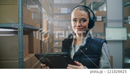 Portrait of Female Logistics Manager Wearing Headset Using Tablet Computer, Looking at Camera 121826625