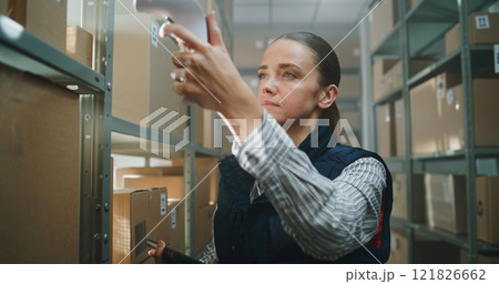 Female Sorting Center Employee Scans Parcel, Checks Information on Tablet Computer 121826662