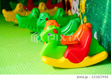 A row of colorful rocking toys in a vibrant and cheerful indoor play area. 121827458