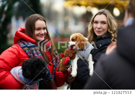 Friends enjoy a winter gathering while holding small dogs in a festive park setting 121827553