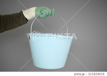 A blue bucket with a handle being held by a gloved hand in a precise manner 121828019