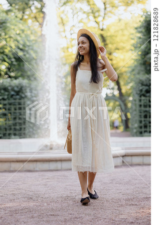 full-length happy African American woman in white dress and straw hat and bag, posing 121828689