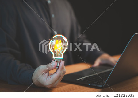 A glowing light bulb held in a person hand, Business concept of no ideas, work hard, tired with business problem solving, with a laptop in the background suggesting modern technology. A glowing light bulb held in a person hand, Business concept of no ideas, work hard, tired with business problem solving, with a laptop in the background suggesting modern technology. 121828935