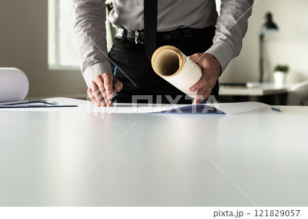 Businessman analyzing plans while working at his desk 121829057