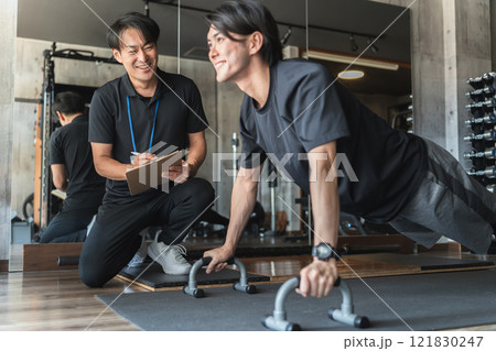 スポーツジムでパーソナルトレーニングを受ける若いアジア人男性 121830247