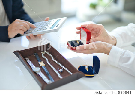 貴金属を査定する買取専門業者とミドル女性の手元 貴金属を査定する買取専門業者とミドル女性の手元 121830841