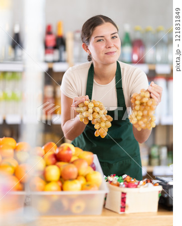 Young woman seller offering grapes in grocery store Young woman seller offering grapes in grocery store 121831849