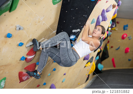 Young woman climbs steep artificial wall in sports complex and trains endurance Young woman climbs steep artificial wall in sports complex and trains endurance 121831882