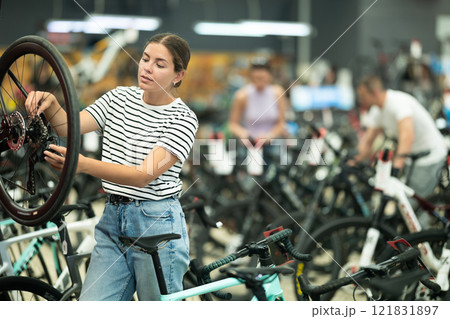 Interested girl inspecting bike wheel and brake system in store Interested girl inspecting bike wheel and brake system in store 121831897