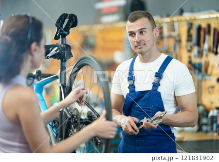 Professional technician examining bike wheel of female client in workshop 121831902