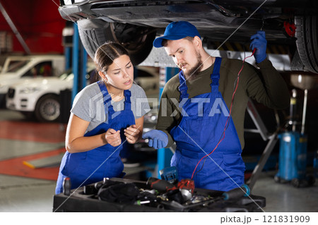 Skilled male auto-mechanic measuring capacity of auto-detail while female worker watching him 121831909