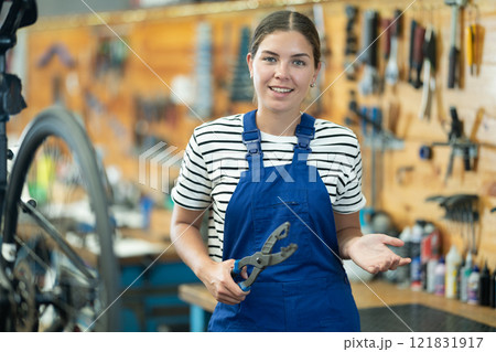 Portrait of young girl master posing with tool, prepared for repair bicycle in sports shop Portrait of young girl master posing with tool, prepared for repair bicycle in sports shop 121831917