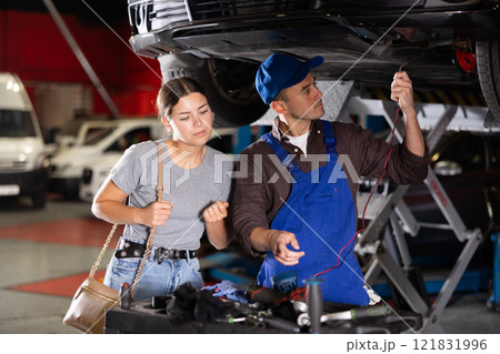 Skilled male auto mechanic measuring capacity of automobile of young girl 121831996