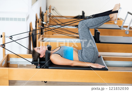 Young girl performing rehabilitation feet-in-strap exercises on Pilates reformer Young girl performing rehabilitation feet-in-strap exercises on Pilates reformer 121832030