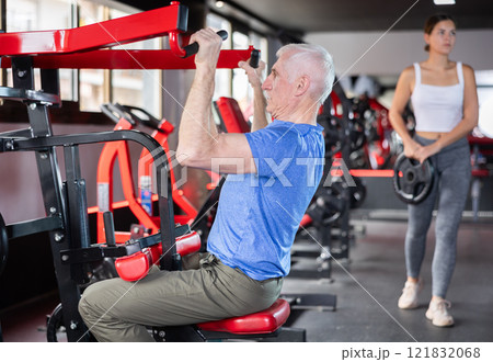 Mature man doing triceps curls in exercise machine during strength training in gym Mature man doing triceps curls in exercise machine during strength training in gym 121832068