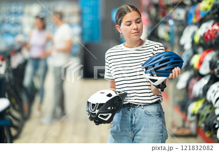 Young woman choosing bicycle helmet in store 121832082
