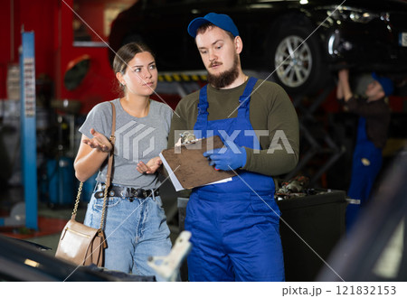 Male worker of auto service speaking to female client concerning his notes on paper 121832153