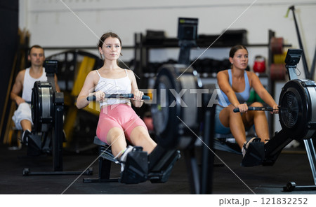 Young woman training at cable row machine with group of sporty people in CrossFit gym Young woman training at cable row machine with group of sporty people in CrossFit gym 121832252