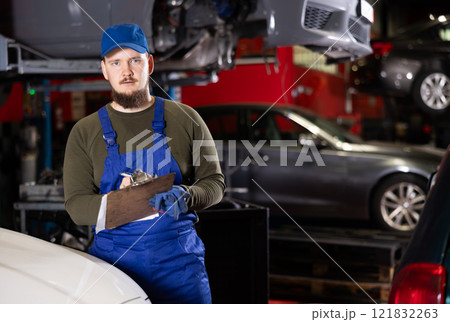 Portrait of professional auto mechanic in uniform with paper holder in car service center 121832263