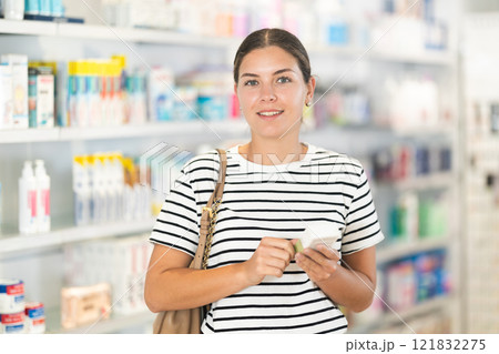 Girl thoughtfully chooses medicines in modern pharmacy 121832275