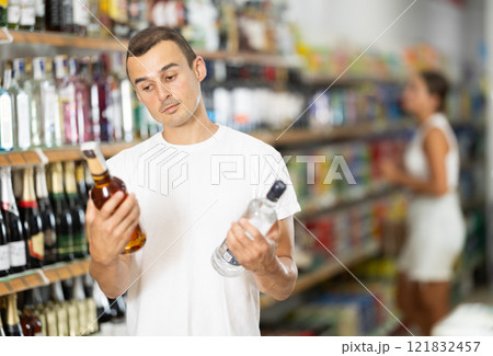 Male shopper selects wodka in produce section of supermarket Male shopper selects wodka in produce section of supermarket 121832457
