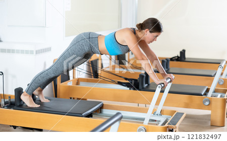Girl doing stretching exercises on reformer in pilates studio 121832497