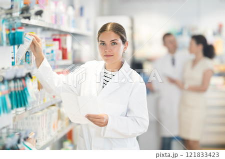 Young female pharmacist choosing convenient medicament in box 121833423