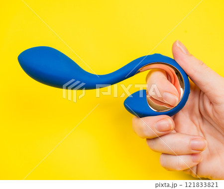 Female hand holding blue vibrator sticking out of yellow paper background. Female hand holding blue vibrator sticking out of yellow paper background. 121833821